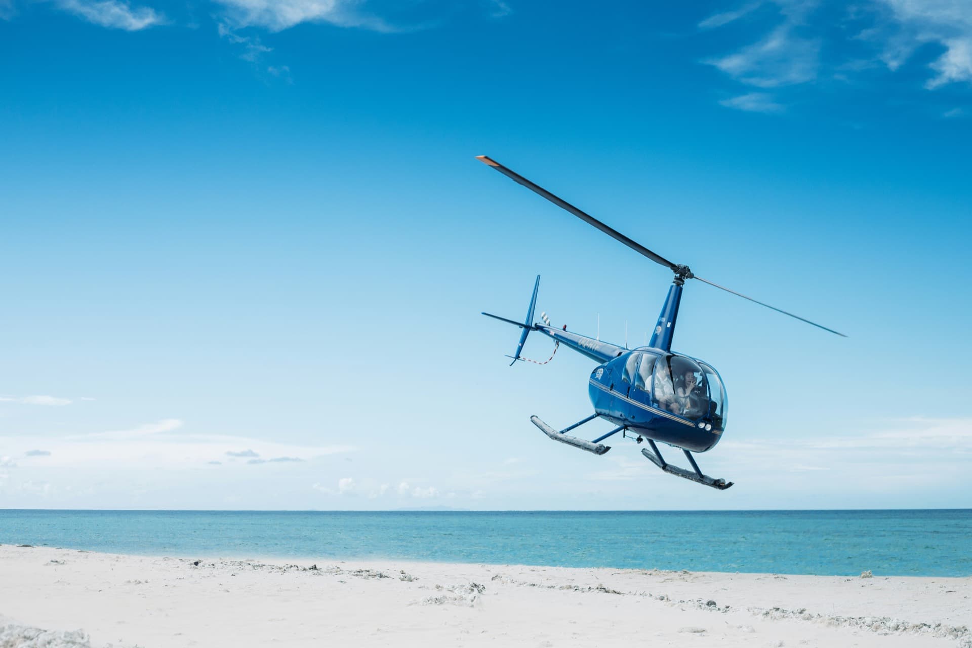 Private helicopter over a white-sand Balearic beach and turquoise sea